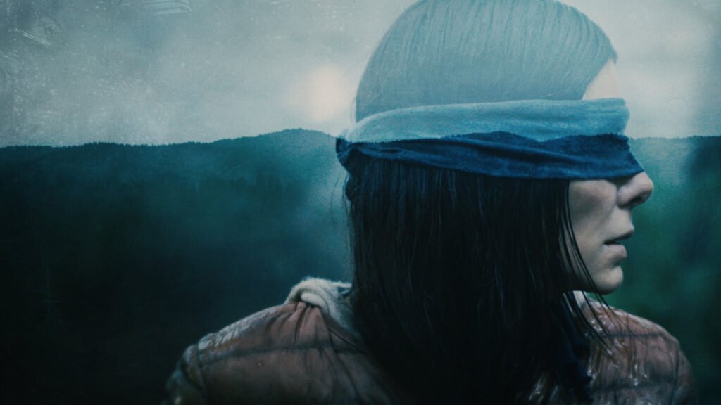 Cena do filme de suspense pós-apocalíptico da Netflix mostrando uma mulher vendada em ambiente externo, com expressão tensa e paisagem enevoada ao fundo; imagem icônica associada ao clima de sobrevivência e mistério da produção.